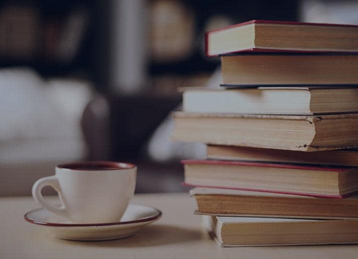 a stack of books next to a coffee cup in a saucer